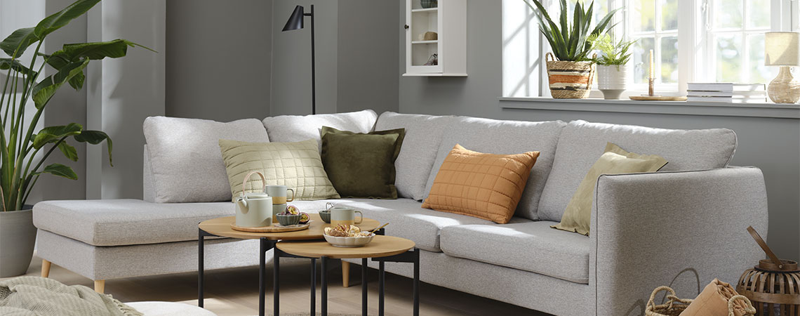 Arredamento soggiorno con divano grigio scuro e cuscini arancioni, verdi e beige