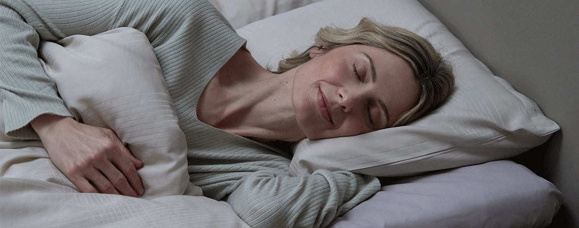 Femme dormant sur le côté dans un lit avec oreiller et couette blancs