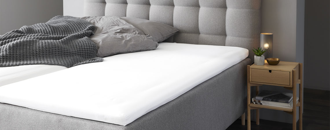Schlafzimmer mit grauem Kingsize-Bett mit Matratzenauflage, grauem Kissen und Duvet.