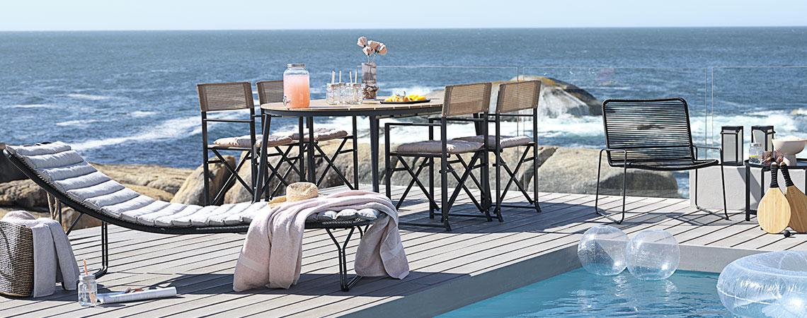 Area lounge con tavolo e sedie da giardino e lettino prendisole a bordo piscina
