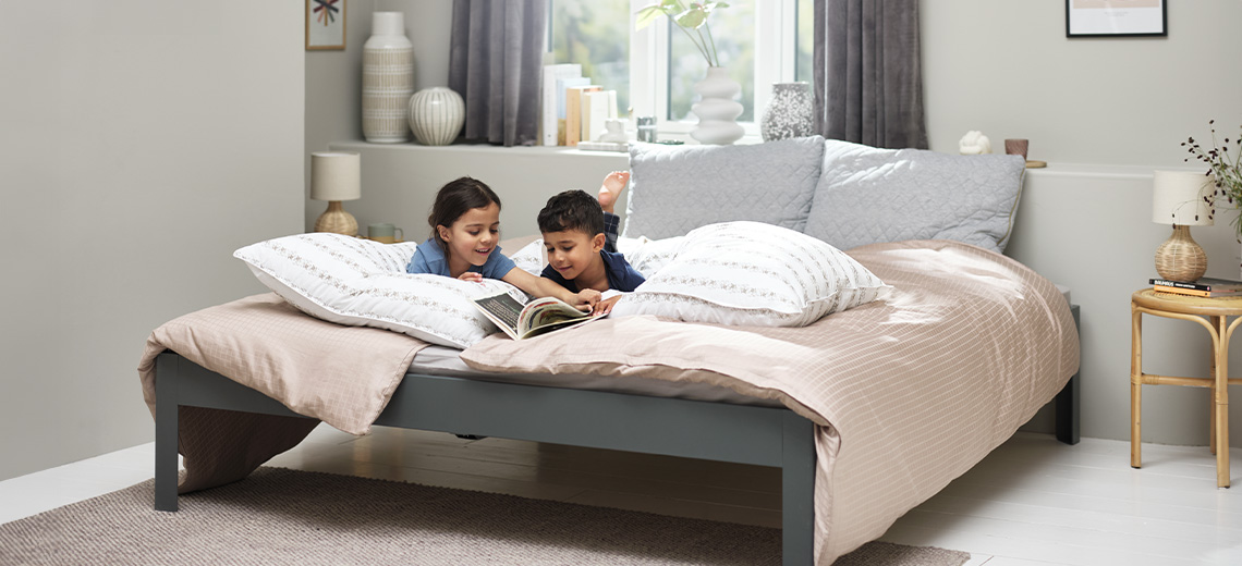 Zwei Kinder lesen ein Buch auf einem Doppelbett mit Duvet, Kopfkissen und Zierkissen