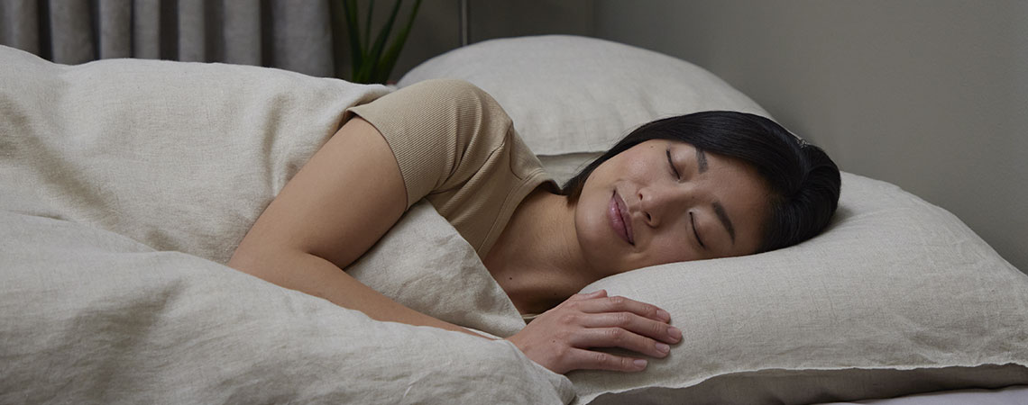 Donna che dorme su un fianco nel letto con un guanciale e un piumino su lenzuola beige