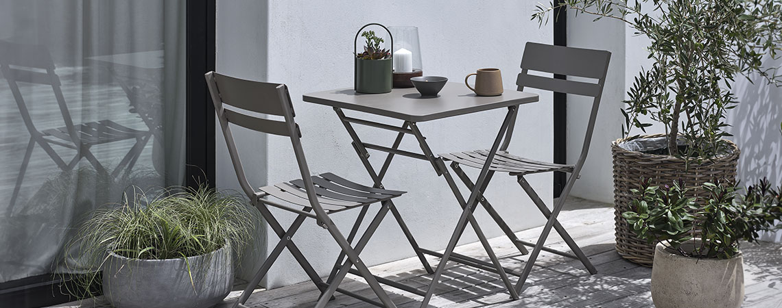 Braunes Bistro-Set auf einem kleinen Balkon mit Pflanzen und Pflanztöpfen