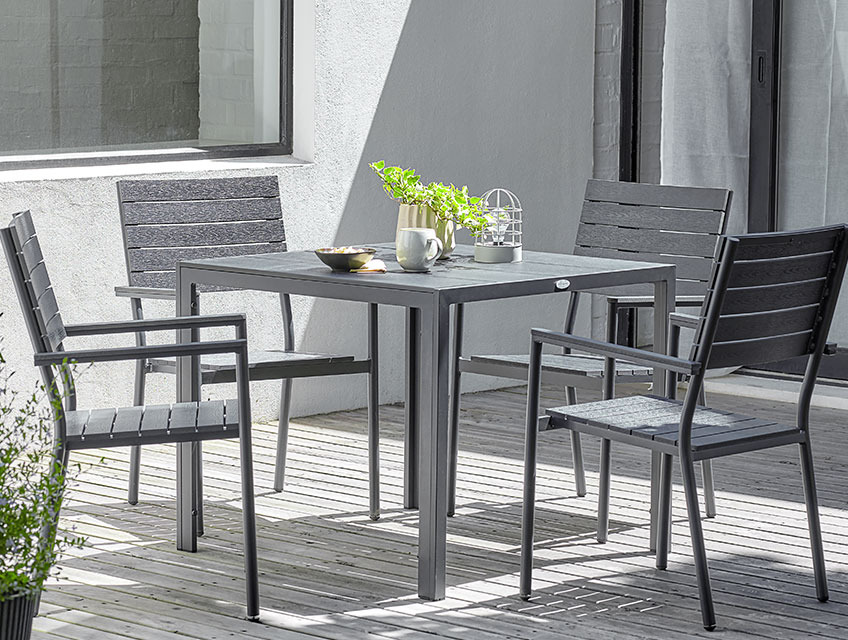 Gartentisch MADERUP und Gartenstühle PADHOLM Quadratischer Gartentisch und vier Stapelstühle auf einer sonnigen Terrasse