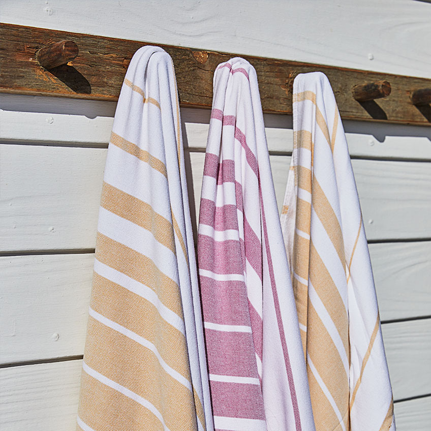 Drei gestreifte Strandtücher in Weiss, Orange und Pink an einer Holzwand aufgehängt