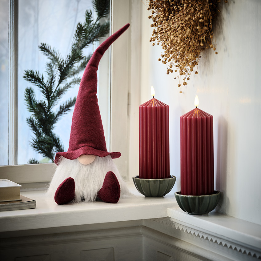 Skandinavischer Weihnachtswichtel neben grossen roten Kerzen 