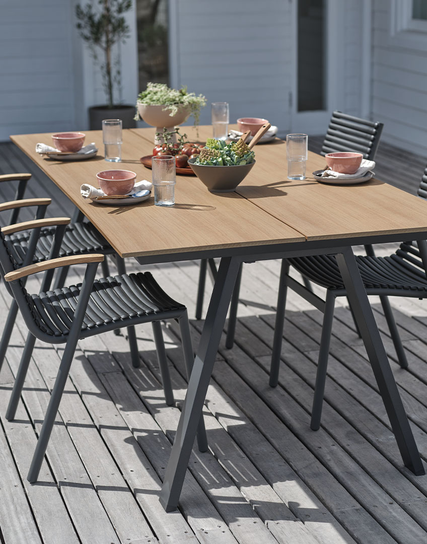 Outdoor-Tisch mit Tischplatte aus Kunstholz und stapelbaren Kunststoffstühlen mit Armlehnen aus recyceltem Teakholz