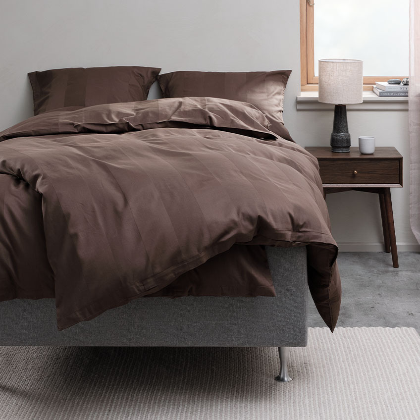 Schokoladenbrauner Bettbezug und Baumwollbettwäsche auf dem Bett im Schlafzimmer