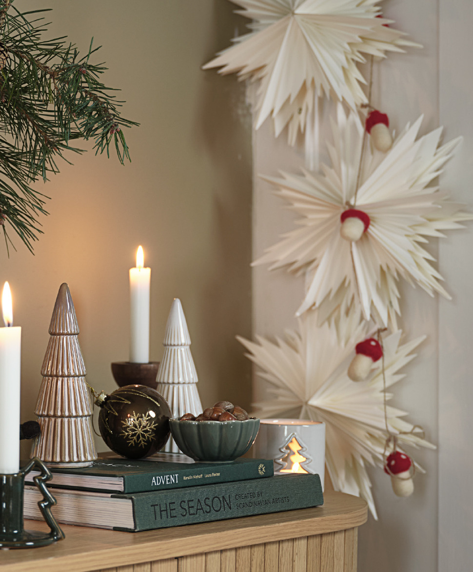 Étoiles en papier SKRYMSLI et champignons en feutre LODUR en guirlande Un buffet avec de belles décorations de Noël et des étoiles en papier le long du mur