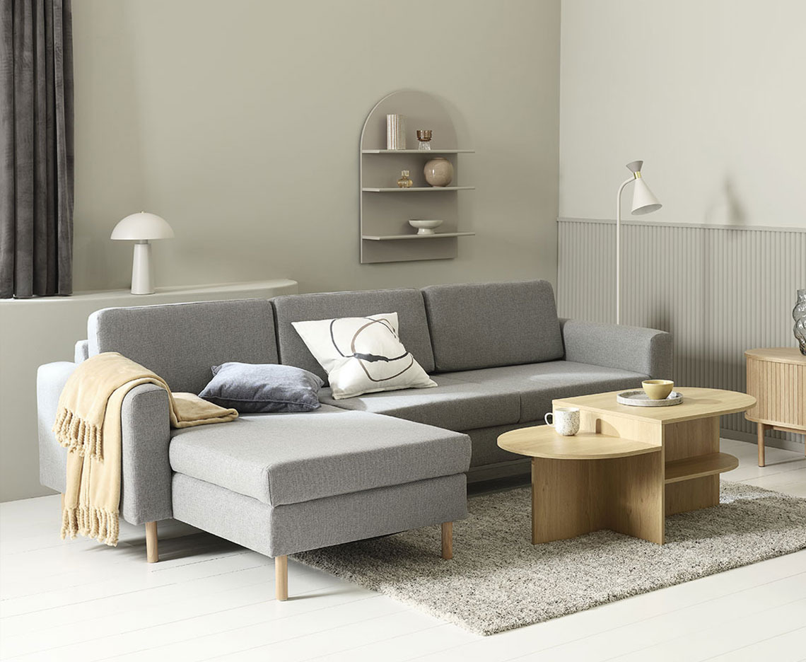 Divano con chaise longue grigio chiaro nel soggiorno con tavolino, lampada e decorazioni per la casa