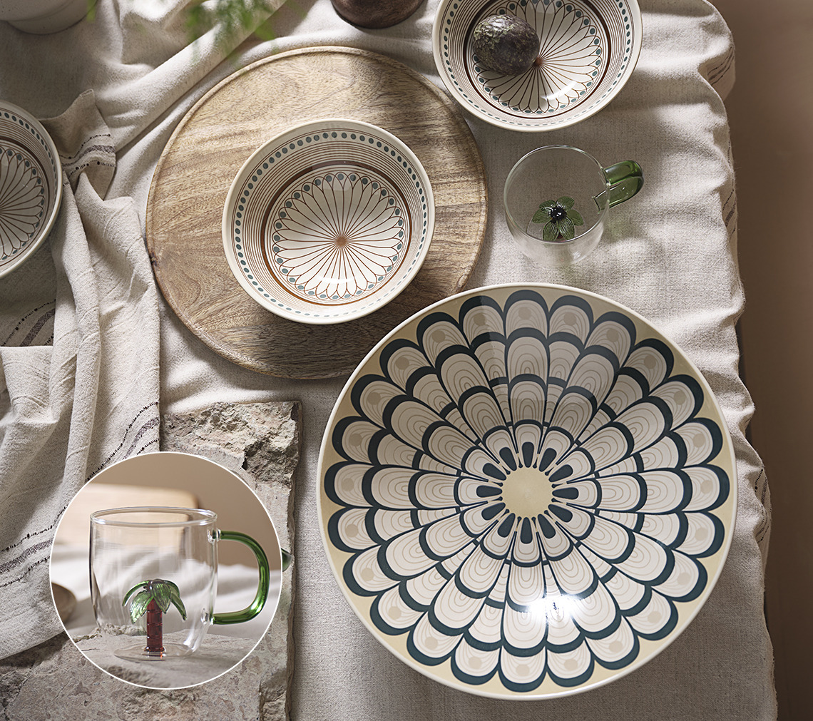 Table dressée avec une nappe, un grand bol, un petit bol ainsi qu’une tasse en verre avec un palmier.