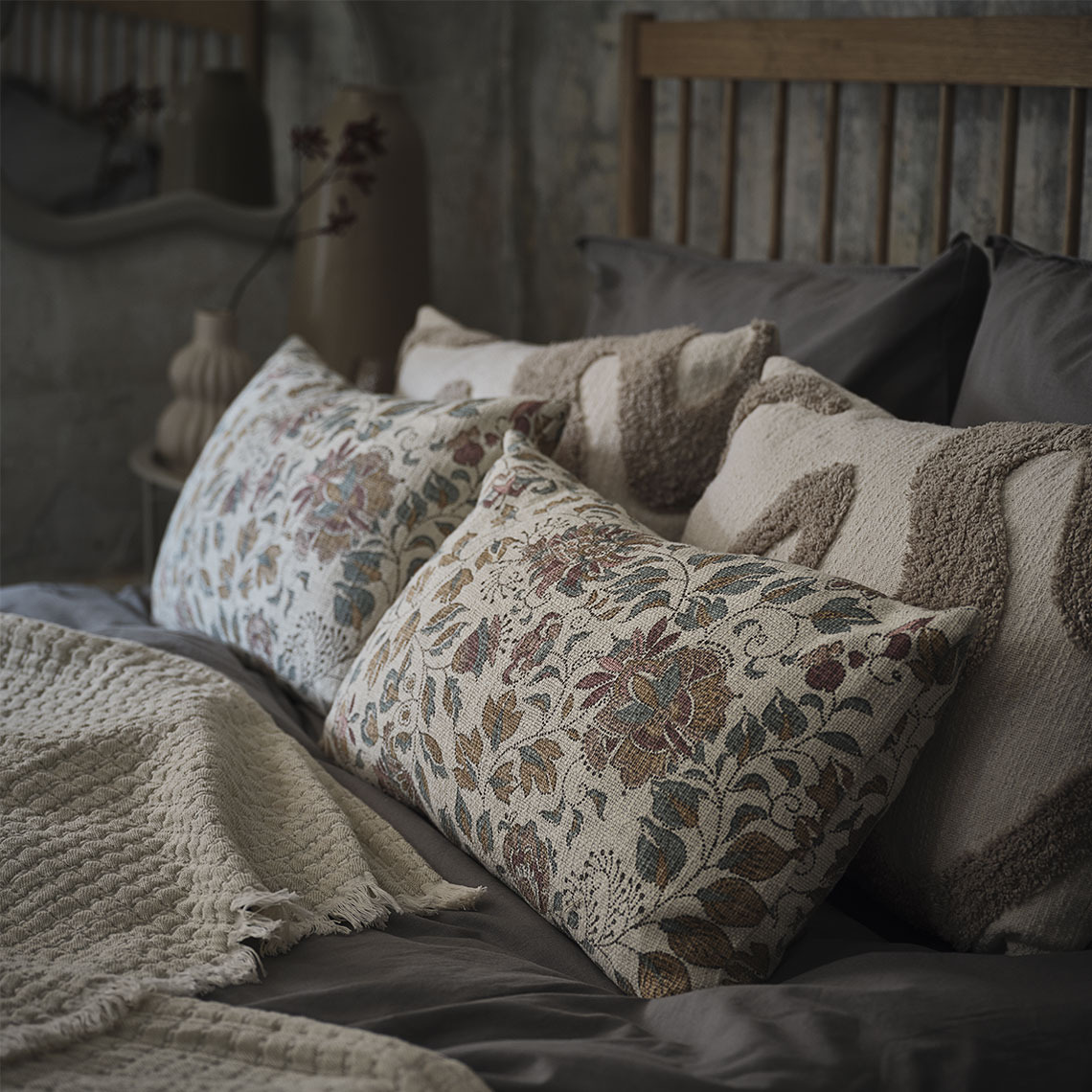 Kissen in Beige mit Blumenmotiv auf einem Bett, das von einer beigen Decke geschmückt wird.