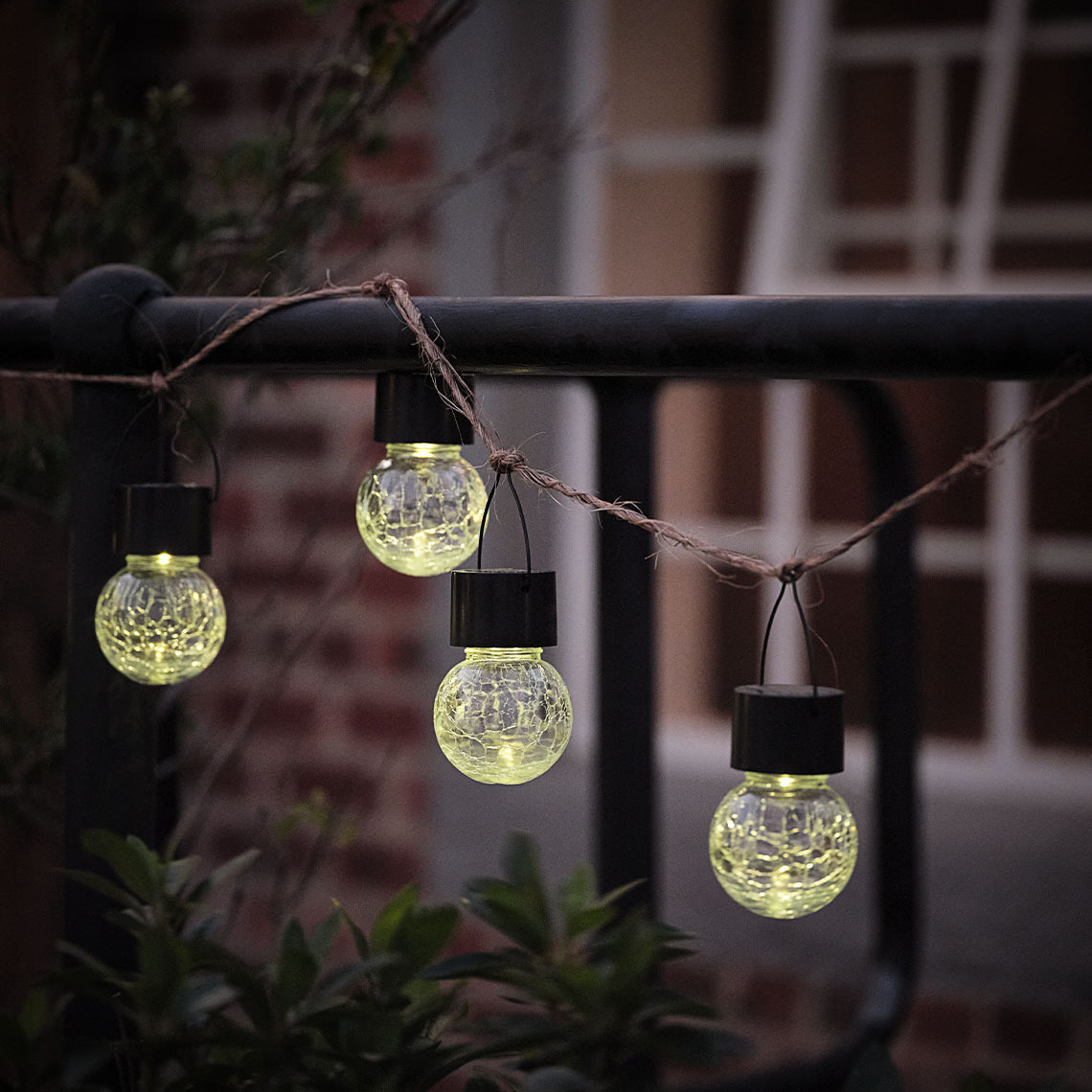  Eine kleine Solar-Gartenleuchte hängt an einer Schnur entlang eines Zauns