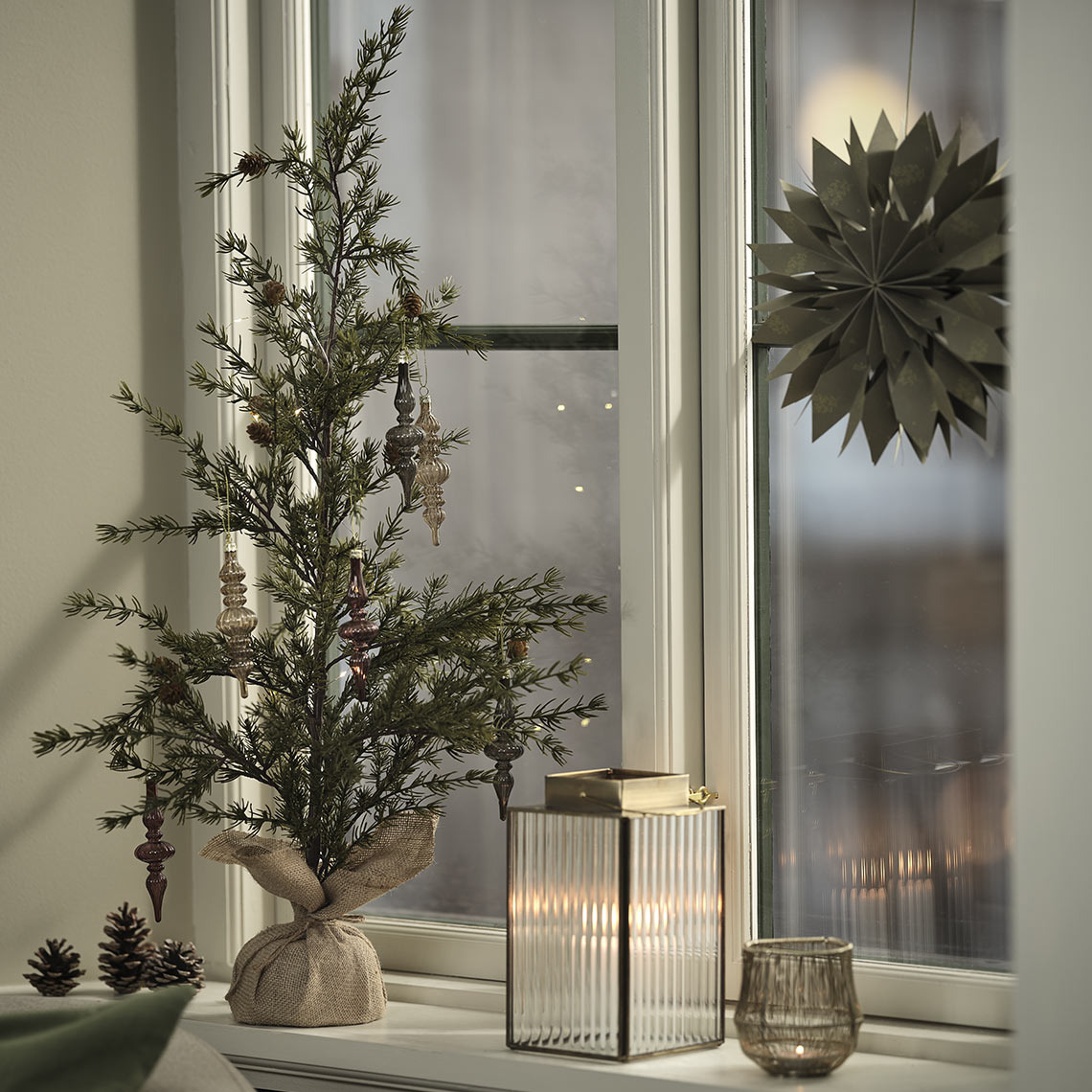 Teelichthalter, Laterne und künstlicher Weihnachtsbaum mit Dekorationen auf der Fensterbank