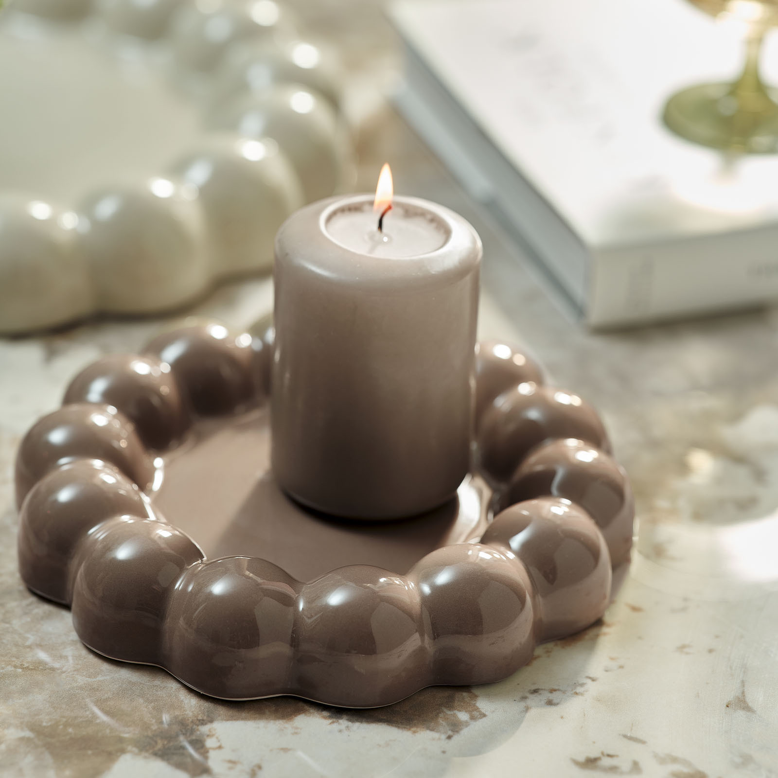 Candela su un vassoio decorativo marrone con bordo decorato a pon pon