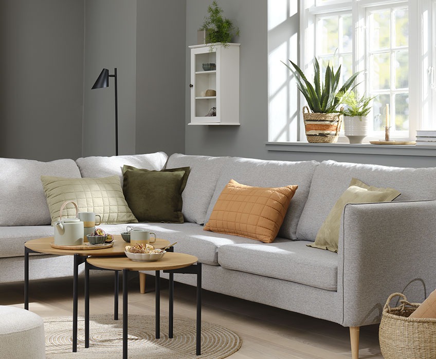 Wohnzimmereinrichtung mit grauem Sofa und orange-, grün- und beigefarbenen Zierkissen