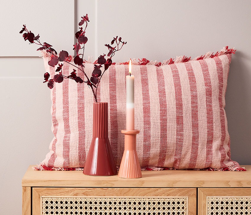 Gestreiftes Kissen hinter roter Vase und Kerzenständer mit gestreifter Kerze