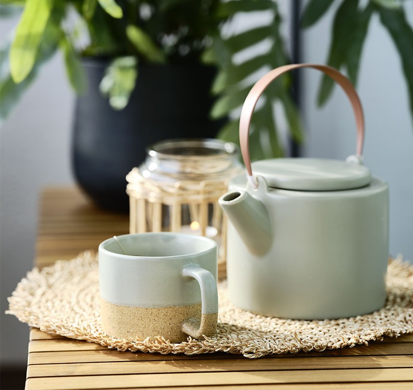 Teekanne und Tasse auf einer Gartenbank serviert