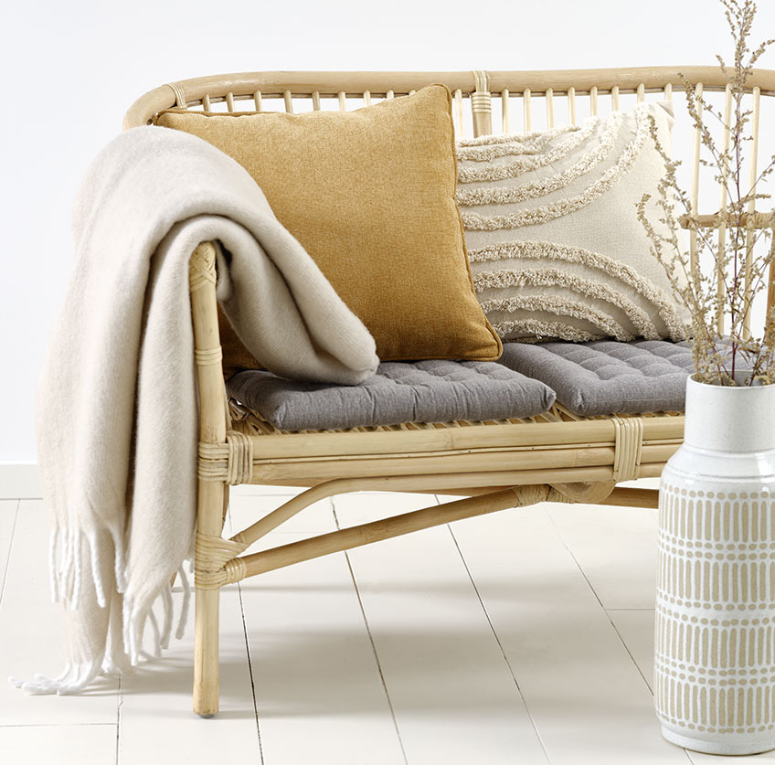 Rattansofa LISELEJE mit beigem Zierkissen GRAVMYRT, gelbem Zierkissen HORNFIOL und Kuscheldecke TUSENFRYD Sofa aus Rattan mit beigen und gelben Zierkissen und beiger Wohndecke