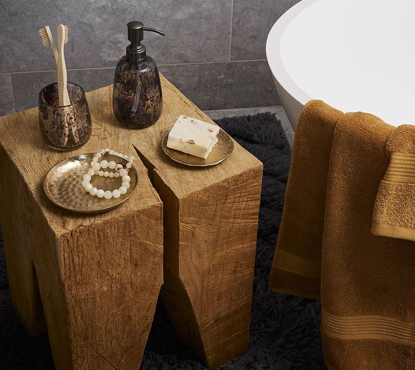 Grosser Holzblock mit zwei goldenen Deko-Tabletts, Zahnbürstenhalter und Seifenspender in einem Badezimmer 