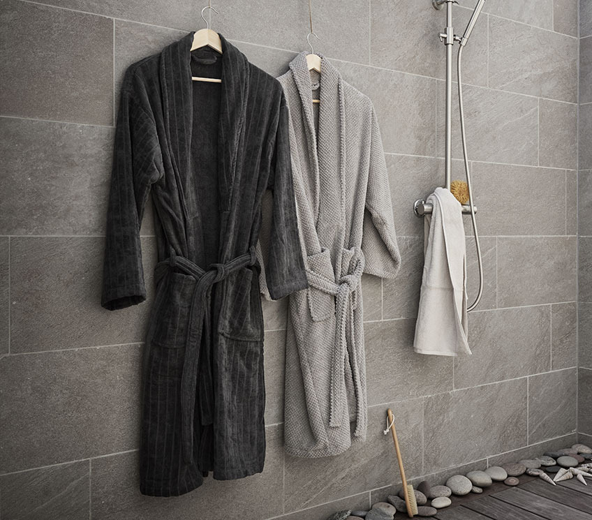 Badezimmer mit zwei grauen Bademänteln, weissem Handtuch und einer Badebürste