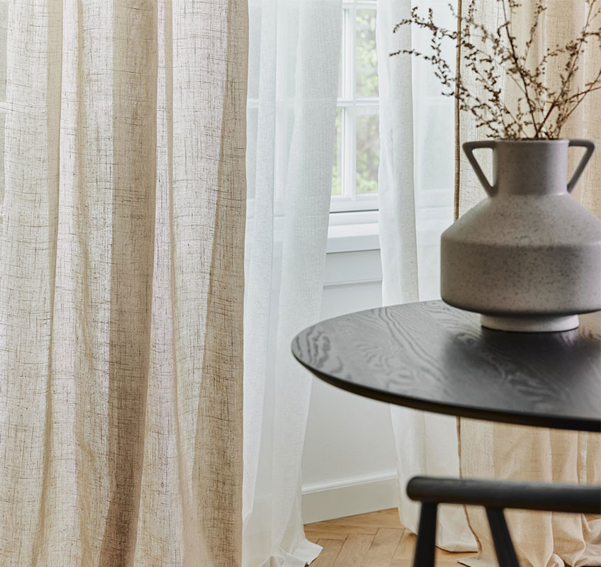 Durchsichtige Vorhänge in Khaki und Weiss vor einem Fenster, Vase auf einem schwarzen Tisch