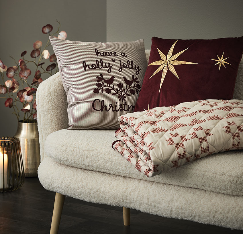 Zierkissen NIDHUG und RIND, Steppdecke TRILOBIT auf dem Sofa GISTRUP Zierkissen und Steppdecke mit Weihnachtsmotiven auf einem weissen Sofa
