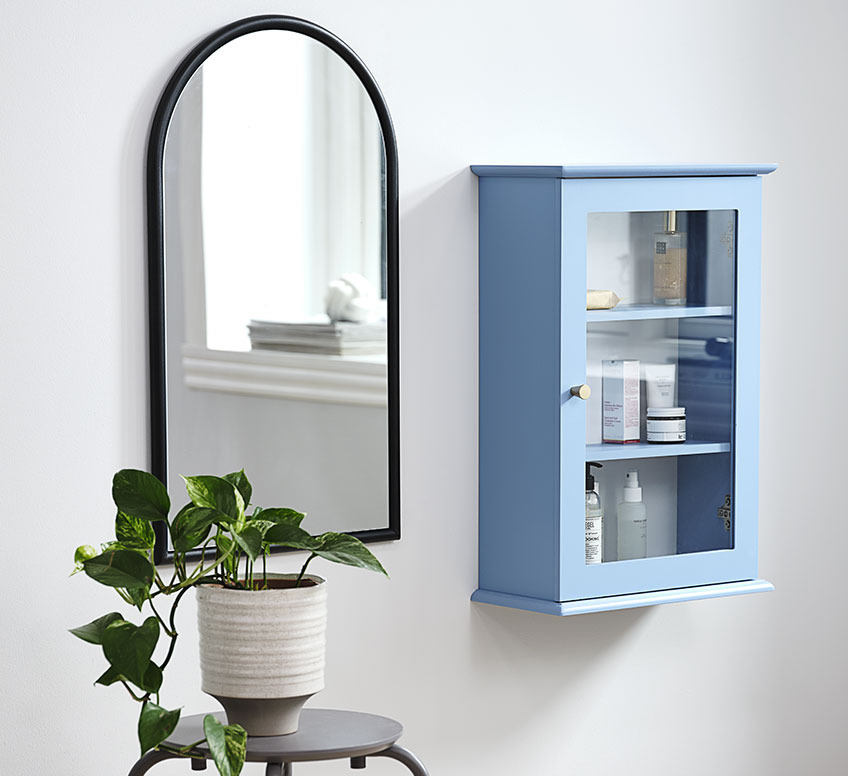 Spiegel mit schwarzem Rahmen neben einem kleinen blauen Hängeschrank 