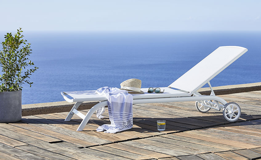Weisse Sonnenliege mit Rädern auf einer Terrasse neben dem Meer