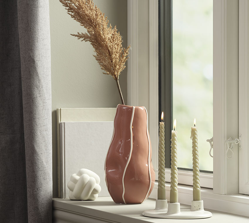 Weisse Skulptur, altrosafarbene Vase und weisser Kerzenständer mit drei Stabkerzen auf einer Fensterbank