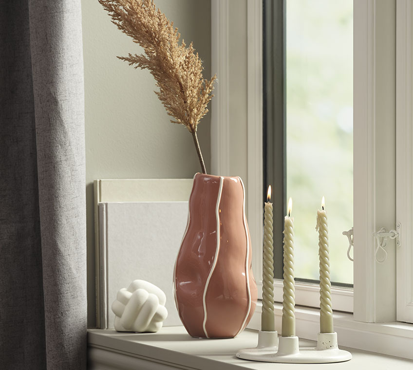 Skulptur HAUGE, Vase ULF und Kerzenständer LAURITS Weisse Skulptur, altrosafarbene Vase und weisser Kerzenständer mit drei Stabkerzen auf einer Fensterbank