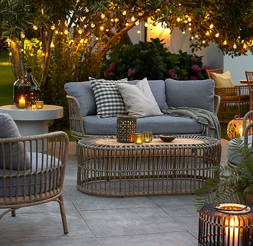 Comodi mobili da lounge sul patio con luci a stringa, lampade a batteria e lanterne con candele e lumini